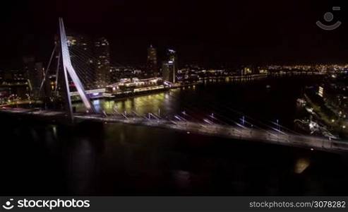 Timelapse shot of car traffic on illuminated Erasmus Bridge and boats sailing down the river in Rotterdam, view at night