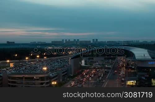 Timelapse shot of city with car stream on the road and full multilevel parking lot near Sheremetyevo Airport, Moscow. View from late evening to night