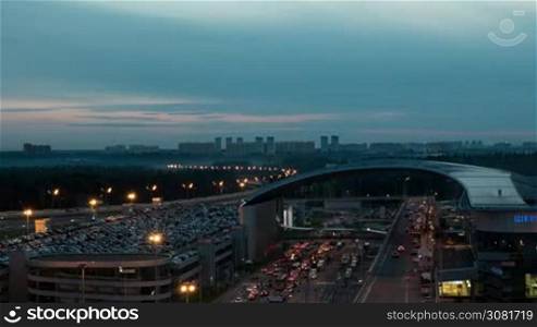Timelapse shot of city with car stream on the road and full multilevel parking lot near Sheremetyevo Airport, Moscow. View from late evening to night