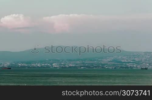 Timelapse shot of growing dusk. Clouds gathering over the quiet sea and distant coastal city