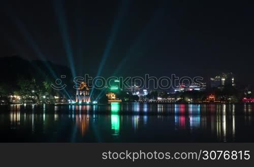 Timelapse shot of Hanoi at night. Illuminated Turtle Tower and Hoan Kiem Lake in city centre. Colorful lights reflecting in dark water, Vietnam