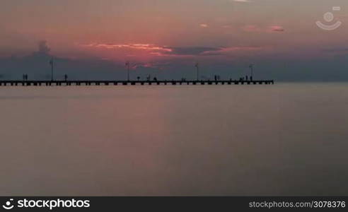 Timelapse shot of people on distant pier, sea and clouds. Evening coming and it getting dark