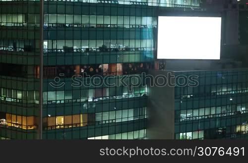 Timelapse shot of people working in business centre and big blank advertising screen on the building at night. Seoul, South Korea