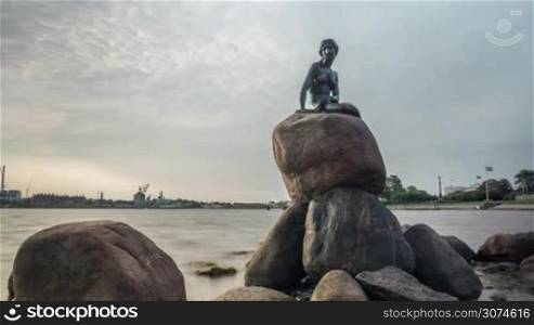 Timelapse shot of rippling water and cloud moving over the Little Mermaid statue on the rock. Famous bronze statue in Copenhagen, Denmark