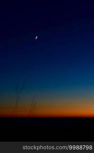 Tiny crescent moon in the blue sky just after sunset