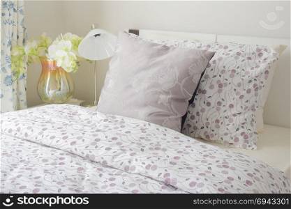 Tiny lavender pattern style bedding in bedroom with white orchid next to bed.