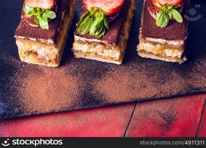 Tiramisu cake on black slate and red wooden background