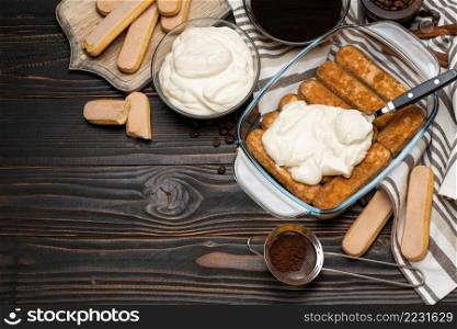 tiramisu dessert cooking - Traditional Italian Savoiardi ladyfingers Biscuits and cream in glass baking dish and coffee on wooden background or table. tiramisu dessert cooking - Traditional Italian Savoiardi ladyfingers Biscuits and cream in glass baking dish and coffee on wooden background
