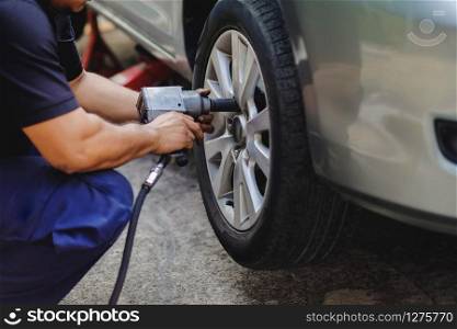 Tire Replacement concept. Mechanic Using Electric Screwdriver Wrench for Wheel Nuts in Garage. Car Maintenance and services