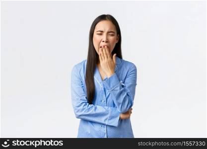 Tired and bored cute asian girl in blue pajamas yawning from boring stories at sleepover party, got exhausted, showing lack of interest, standing over white background wanna go sleep.. Tired and bored cute asian girl in blue pajamas yawning from boring stories at sleepover party, got exhausted, showing lack of interest, standing over white background wanna go sleep