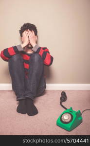 Tired and sad young man is sitting on the floor with a telephone