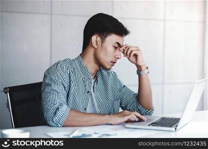 Tired and Stress Young Businessman Sitting on Desk in Office with Computer Laptop. Man Massaging a Nose and Closed Eyes, Keeping Calm and Relax from Hard Work