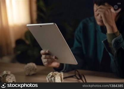 Tired and Stressed Person Sitting on Desk with Tablet in House. Hand on head. Depressed from Work or Some Crisis