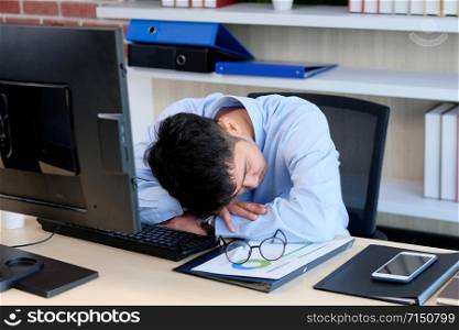 Tired asian man sleeping at office desk. Young businessman with eyeglasses overworked and fell asleep, Creative casual man sleeping at his working place