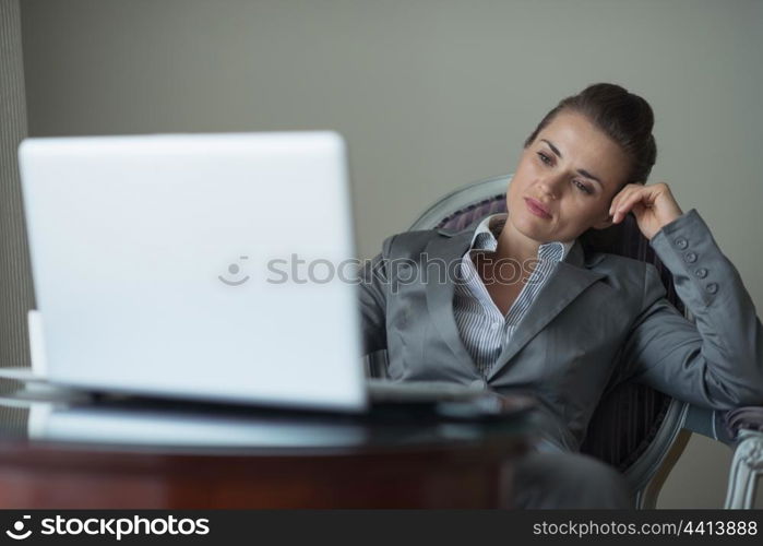 Tired business woman sitting in hotel room and looking on laptop