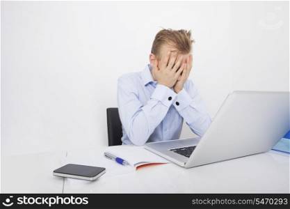 Tired businessman with hands on face sitting at desk by laptop