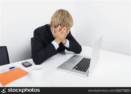 Tired businessman with hands on face sitting at desk by laptop