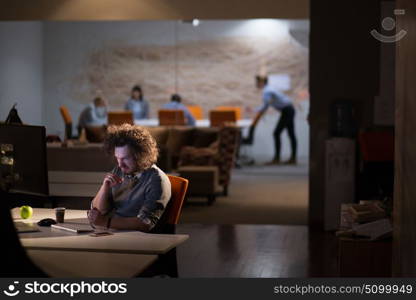 Tired businessman working late doing overtime in office at night drinking coffee to go on.