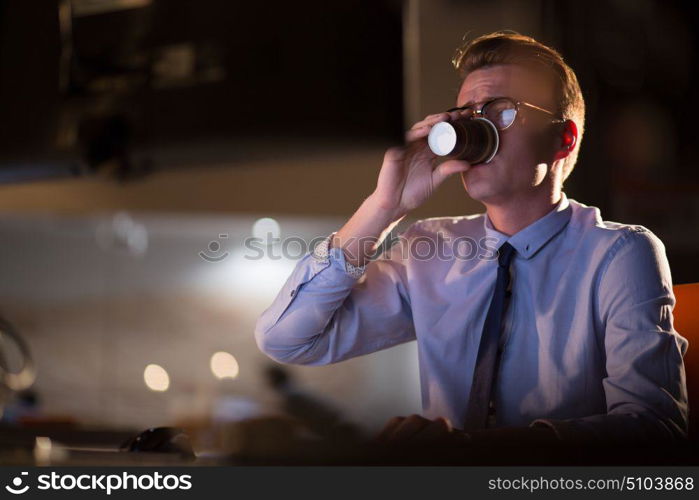 Tired businessman working late doing overtime in office at night drinking coffee to go on.