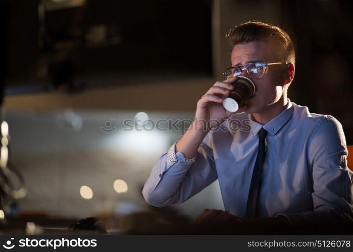 Tired businessman working late doing overtime in office at night drinking coffee to go on.