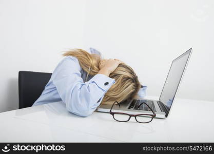 Tired businesswoman resting head on laptop in office