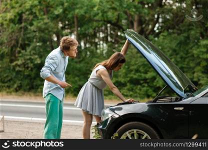 Tired couple at the opened hood on road, car breakdown. Broken automobile or emergency accident with vehicle, trouble with engine on highway. Tired couple at the opened hood, car breakdown