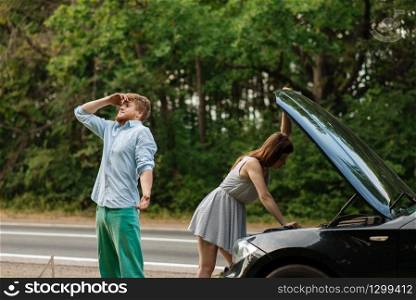 Tired couple at the opened hood on road, car breakdown. Broken automobile or emergency accident with vehicle, trouble with engine on highway