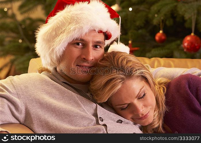 Tired Couple Relaxing In Front Of Christmas Tree