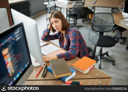 Tired female IT specialist works on computer in office. Web programmer or designer at workplace, creative occupation. Modern information technology, corporate team. Tired IT specialist works on computer in office