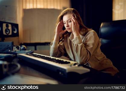 Tired female sound engineer in headphones, recording studio interior on background. Synthesizer and audio mixer, musician workplace, hard creative process. Tired female sound engineer, hard creative process