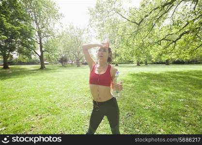 Tired fit woman with water bottle listening to music in park