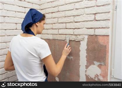 Tired girl performs work on the imitation of brickwork on the wall