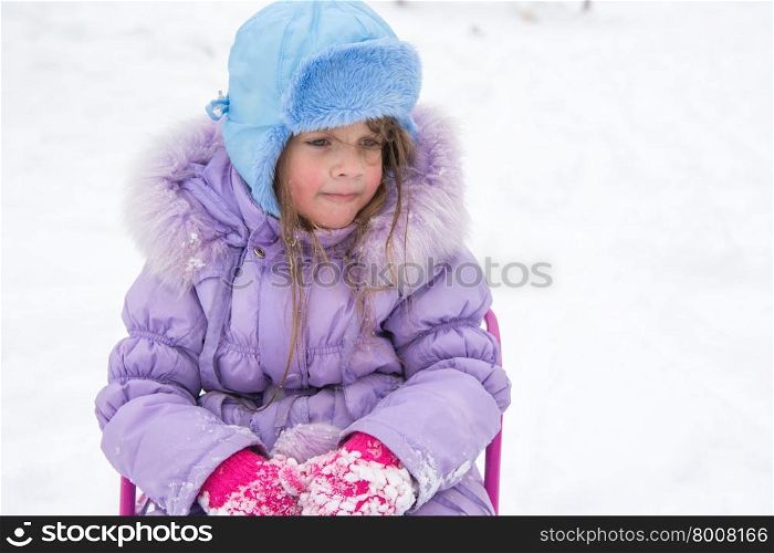Tired girl sitting on a sled. Tired and disheveled walk up five year old girl sitting on a sled
