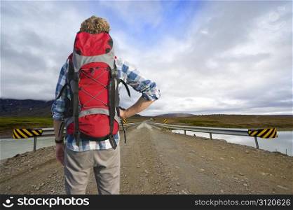Tired Hiker , with a defeated pose, looks across a bridge at the bus home, leaving from the middle of nowhere.
