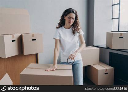 Tired hispanic woman packs cardboard boxes using duct tape. Overworked female employee packs parcels with goods with adhesive sellotape, frowning. Overtime, delivery service concept.. Tired hispanic woman packs parcels boxes using duct tape, frowning. Overtime, delivery service