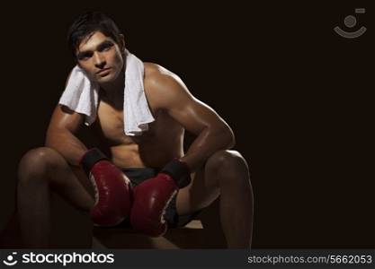 Tired male boxer sitting on stool while looking away over black background