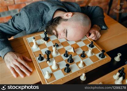 Tired male chess player sleeping on the board. Chessplayer playing, intellectual tournament indoors. Chessboard on wooden table, strategy game. Tired male chess player sleeping on the board