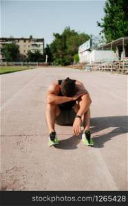 Tired male runner rubbing his forehead while resting after workout, muscular athlete resting after fit training. Tired young athletic man in sportswear lying on the lanes of a running track taking a break from training