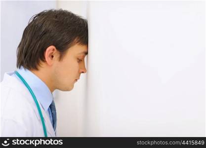 Tired medical doctor leaned his head into a wall