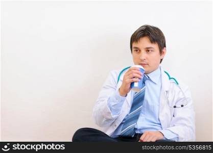 Tired medical doctor sitting on floor with coffee