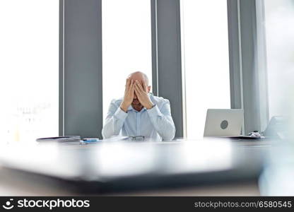 Tired mid adult businessman covering face at desk in office