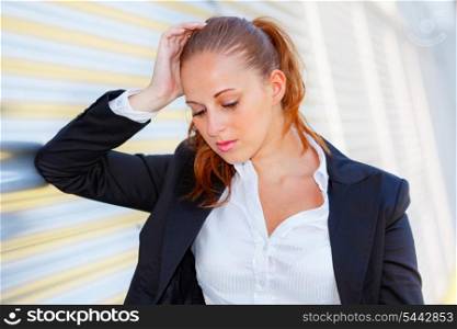 Tired modern business woman standing at office building and looking down&#xA;