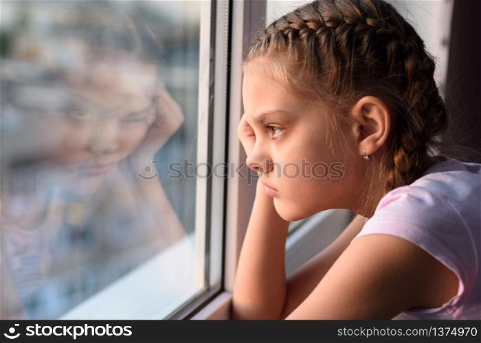 Tired of self-isolation, a bored quarantine girl looks out the window