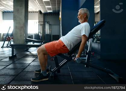 Tired old man with towel leisures after workout, gym interior on background. Sportive grandpa on fitness training in sport center. Healty lifestyle, health care, elderly sportsman. Tired old man with towel leisures after workout