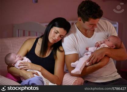 Tired Parents Cuddling Twin Baby Daughters In Nursery