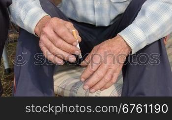 Tired scraped hands of elderly farmer with cigarette