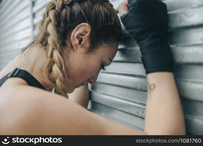 Tired sportswoman resting supported on a metal wall outdoors. Tired sportswoman resting on a metal wall