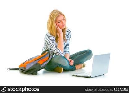 Tired teen girl sitting on floor with backpack and looking on laptop isolated on white &#xA;