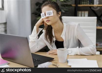 tired woman covering her eyes with drawn eyes paper
