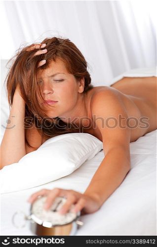 Tired woman holding silver alarm clock lying on white bed
